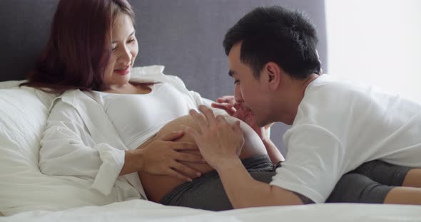 Happy Asian husband and pregnant wife spend time together in the bedroom.