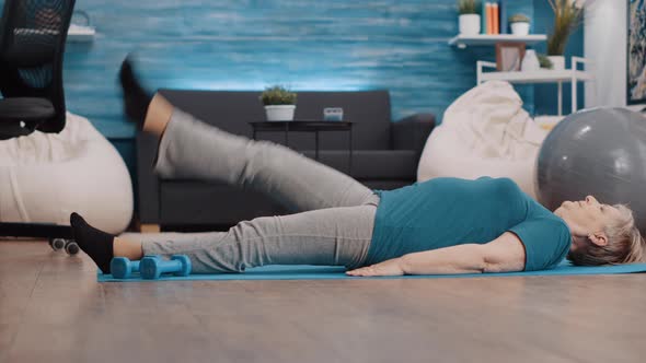 Senior Woman Lifting Legs to Do Physical Exercise on Yoga Mat