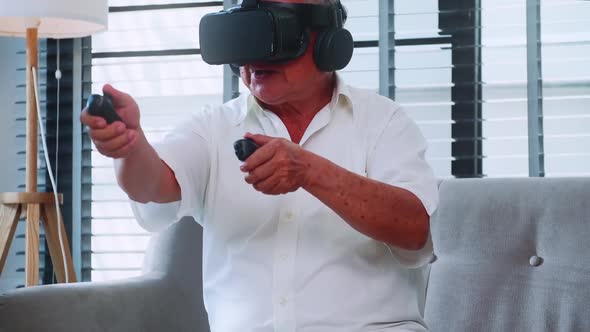 Asian senior man having fun playing video game with virtual reality glasses at home.