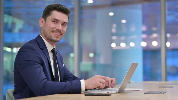 Businessman with Laptop Smiling at Camera in Office