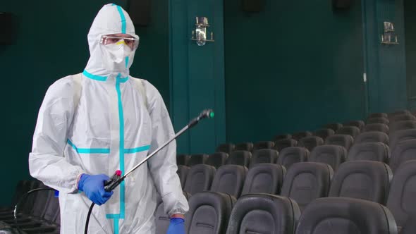 Worker in Antivirus Uniform Spraying Disinfectant at Cinema