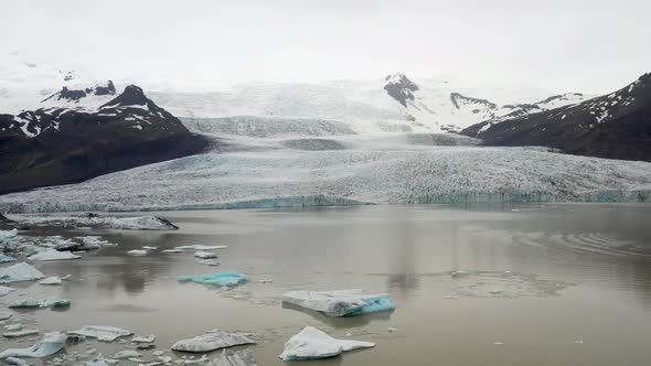 Glacier in Iceland with chunks of blue ice in water with drone video pulling out with wide shot.