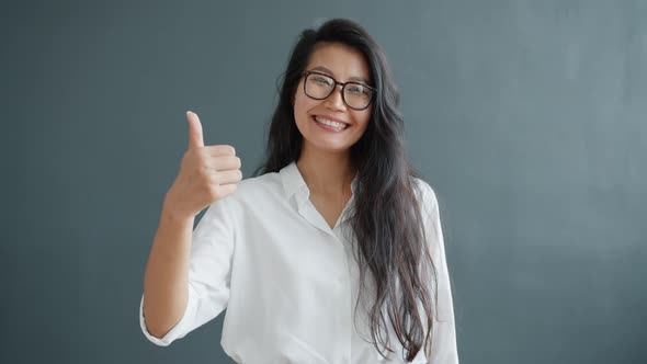 Happy Asian Lady Showing Thumbs-up Hand Gesture on Dark Gray Background