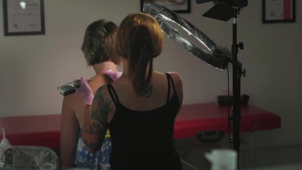 Tattoo-artist makes a tattoo to client's back.Movement of camera to the female's back with design