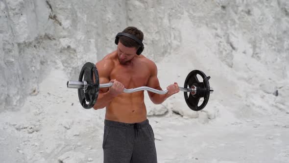 Concentrated muscular man exercising with heavy barbell in the mountains