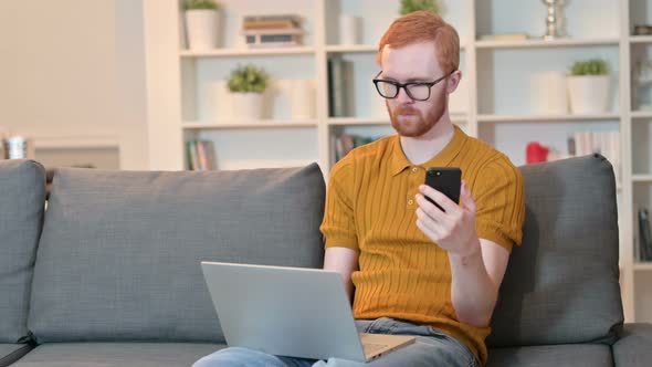 Redhead Man Working on Laptop and Smartphone at Home 