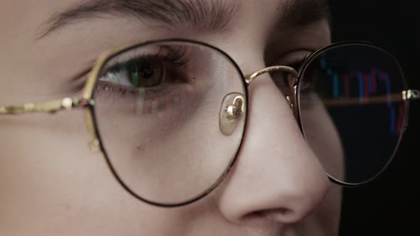 Close up of young woman's face and computer graphing display with glasses.