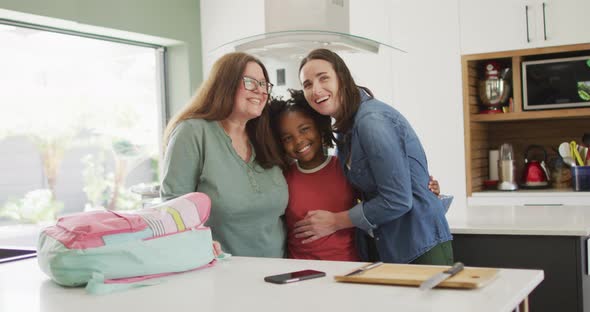 Portrait of happy caucasian lesbian couple and their african american daughter embracing in kitchen