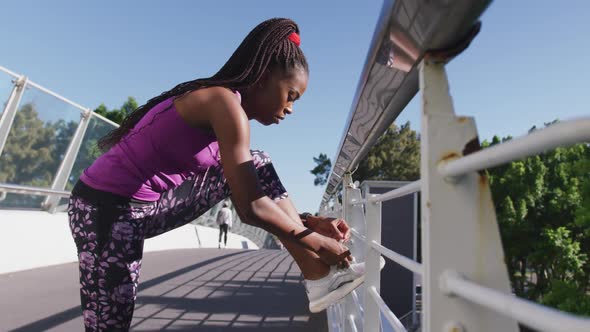 African american woman tying shoe laces on the railing of the city bridge