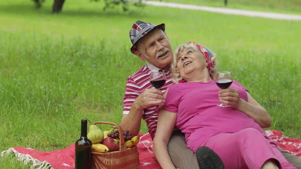 Family Weekend Picnic in Park. Active Senior Old Caucasian Couple Sit on Blanket and Drink Wine