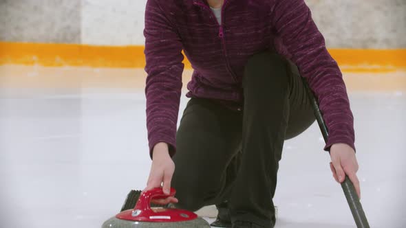 Curling Training on Ice Rink - a Young Woman in Glasses Pushes Off From the Stand with a Stone