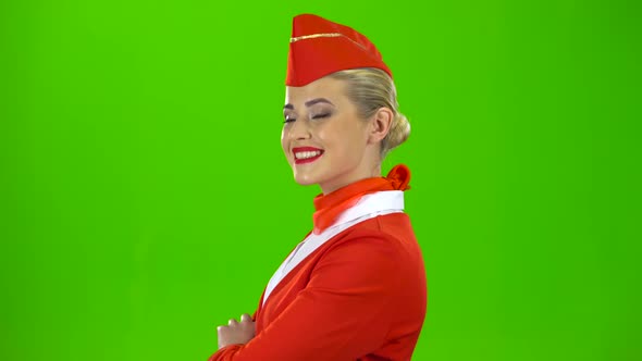 Stewardess in a Red Suit Winks a Slight Flirt. Green Screen. Side View