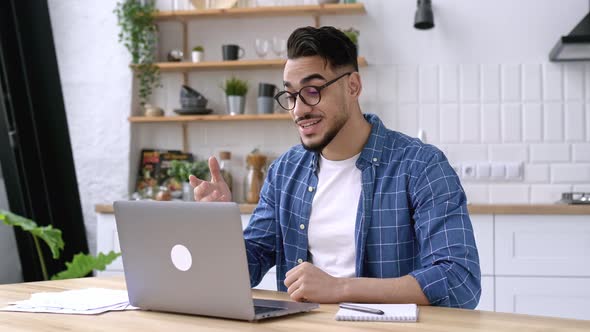 Friendly Happy Arabian or Indian Man with Glasses Sitting at Home in the Kitchen Conducts Video Call