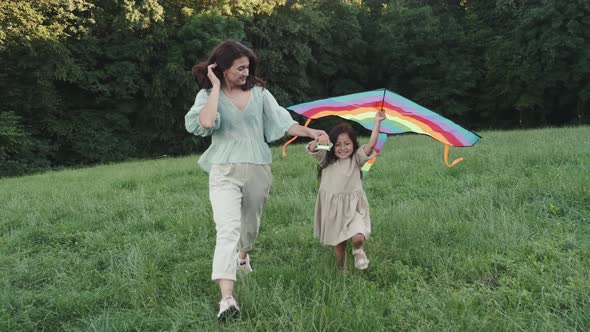 Happy Mother and Daughter Walking with Kite on Lawn