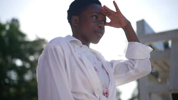 Young African American Woman Holding Hand at Forehead Looking Away in Sunlight