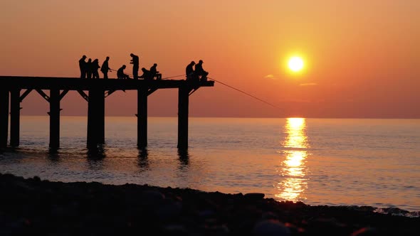 Silhouettes of Fishermen with Fishing Rods at Sea Sunset Sitting on the Pier. Slow Motion.