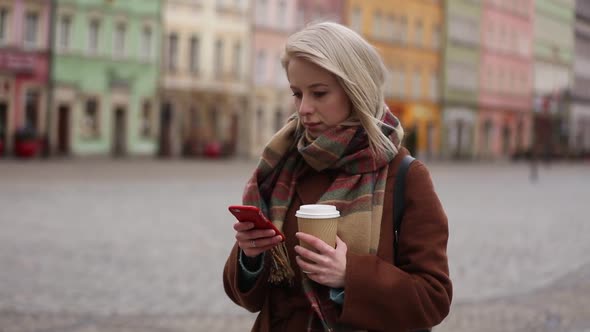 Beautiful woman in coat and scarf with coffee and mobile phone on city street