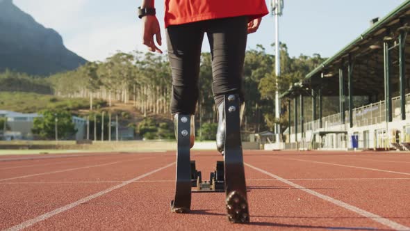 Disabled mixed race man with prosthetic legs walking on racing track towards starting blocks