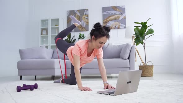 Girl in Sportswear Doing Fitness  with Stretching Strap During Review the Sport Workout on Laptop