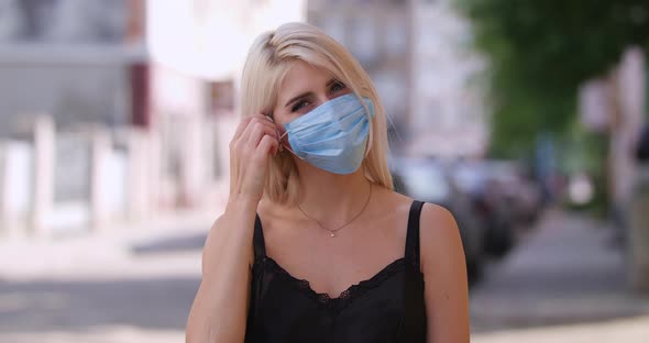 Attractive Young Blonde Woman with Beautiful Blue Eyes Removes the Protective Medical Mask and Looks