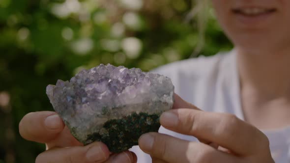 Woman holds crystal quartz stone gemstone performing magic ritual in forest