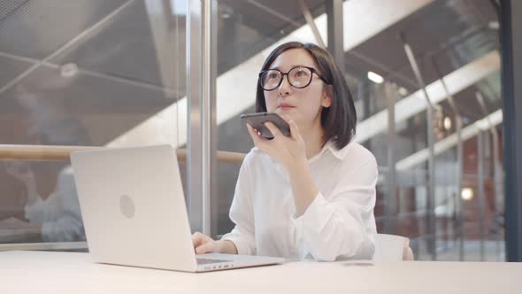 Asian Businesswoman Recording Voice Message on Workplace