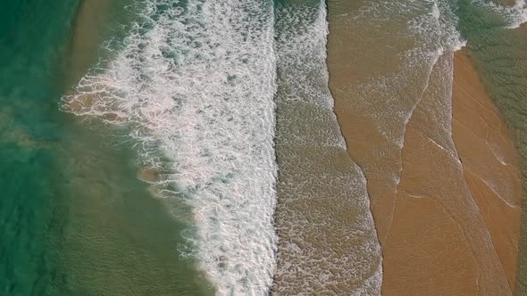 Aerial view of waves breaking over a shallow sand bar close to a popular beach