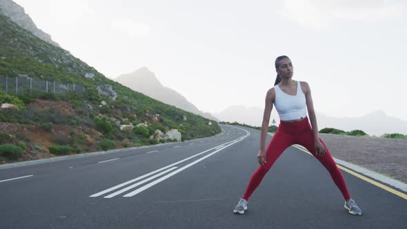 Fit mixed race woman exercising stretching on a country road near mountains