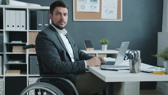 Slow Motion Portrait of Disabled Businessman in Wheelchair Sitting in Office and Looking at Camera