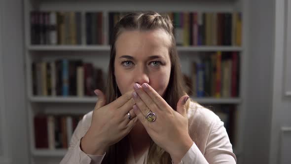 Woman Sitting in Front of Bookshelf and Closes Her Mouth with Hands