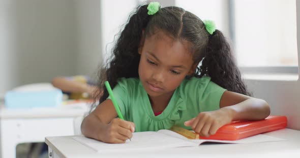 Video of african american girl sitting at desk during lesson in classroom