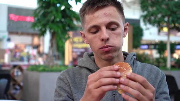 Close Up Shot of a Handsome Caucasian Male Eating a Burger in a Fast Food Restaurant