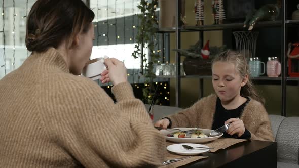 Girl with Long Hair Eats Food Sitting in a Cafe with Her Mother