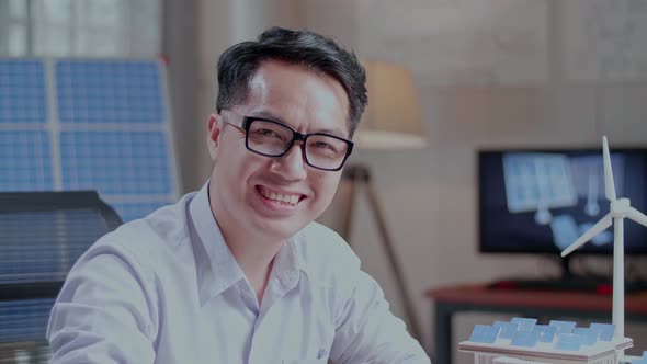 Close Up Of Asian Man Smile To Camera While Working With A Blueprint And The Model Of A Small House