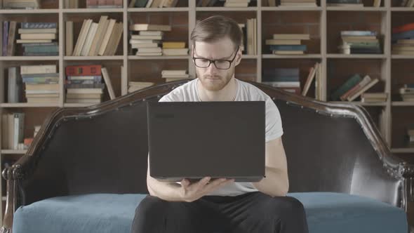 Slowmo Portrait of Serious Absorbed Man Using Laptop in Comfortable Library. Front View of