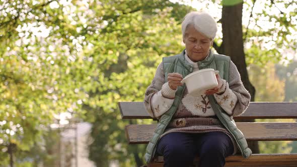 Senior Gray Haired Caucasian Woman Having Lunch Meal in the Park Sitting on the Bench Selective