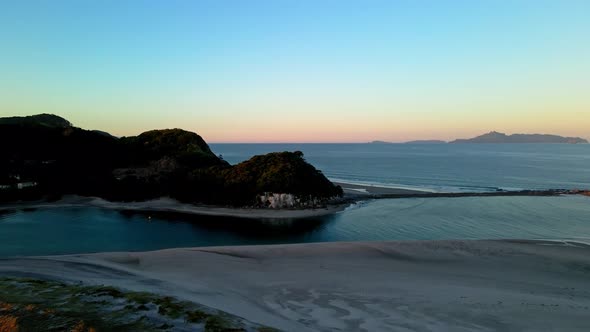Ascending aerial shot showing silhouette of famous Mangawhai Heads during colorful sunset in New Zea