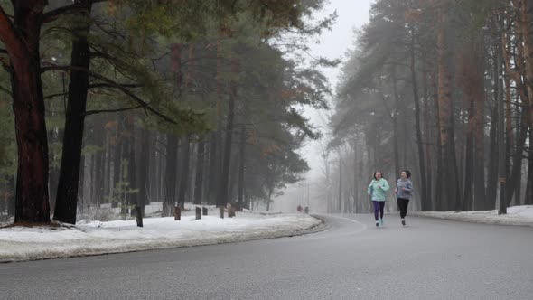 Happy Fit Senior and Young Female Runners Training in Winter Snowy Park Talking and Smiling