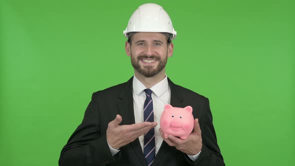 Cheerful Engineer Pointing at Piggy Bank Against Chroma Key