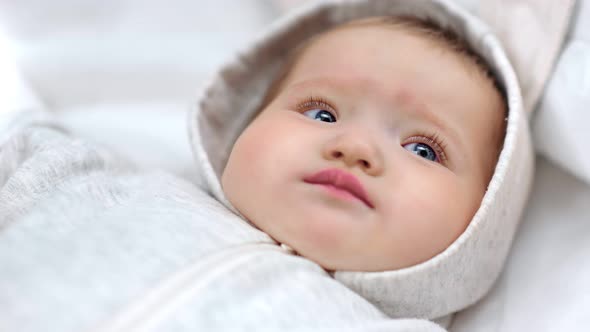 Closeup Face of Cute Little Newborn European Baby Wearing White Overall Having Calmness Emotion