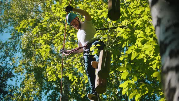 Man Crossing a Construction of the Rope and Stumps and Holding By the Insurance Rope - an