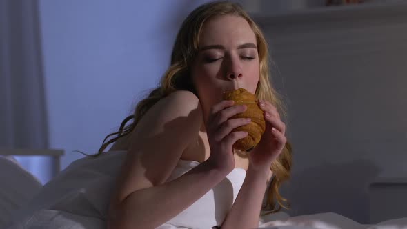 Woman Eating Croissant in Bed at Night, Enjoying Sweets After Diet, Bulimia