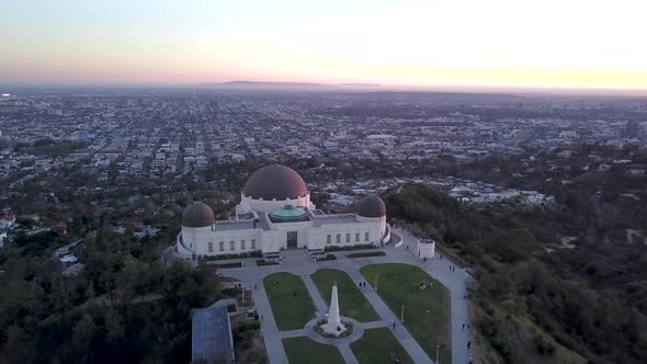 Aerial orbit of the Griffith Observatory and the Los Angeles skyscraper skyline in the background.