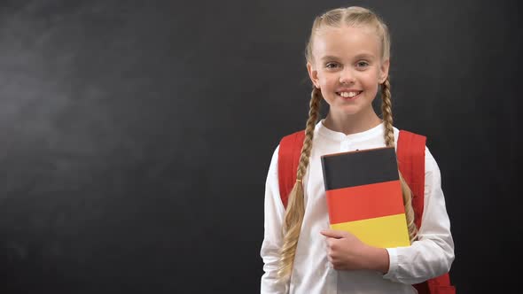 Smiling Female Pupil Holding German Language Textbook, Blackboard Background