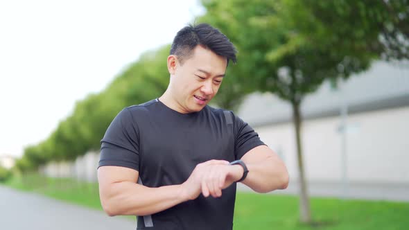 Sport asian man looking smart watch at modern track.