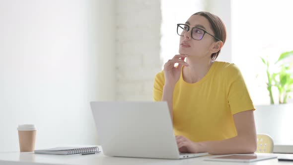 Woman Thinking while Working on Laptop in Office