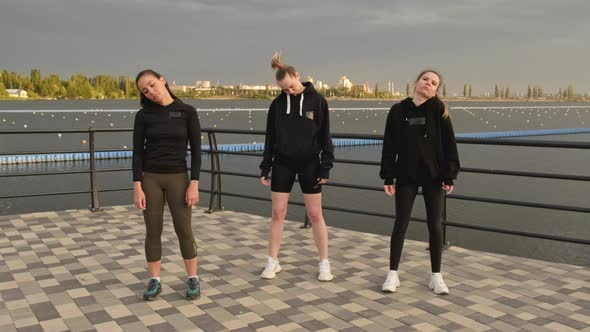 Girls in Black Tracksuits Do a Warmup on the Pier on the Beach