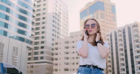 Young Beautiful Woman Talking on the Phone on the Background of Buildings