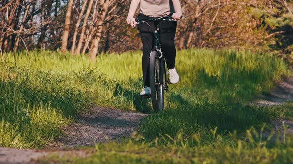 Young Woman on a Bicycle Rides Along Green Forest Path in Sunny Summer Day