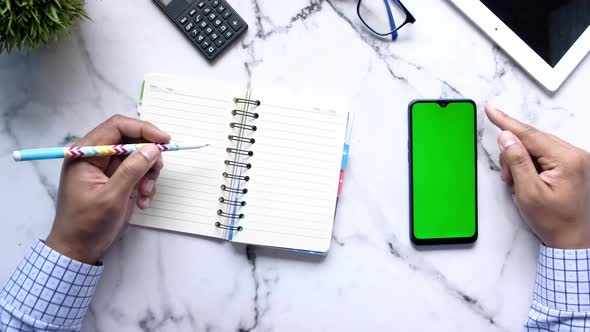 Top View of Man Hand Using Smart Phone and Writing on Notepad